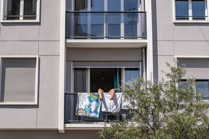 Canicule 2025 : une personne cherche la fraîcheur sur son balcon, les jambes relevées derrière du linge étendu