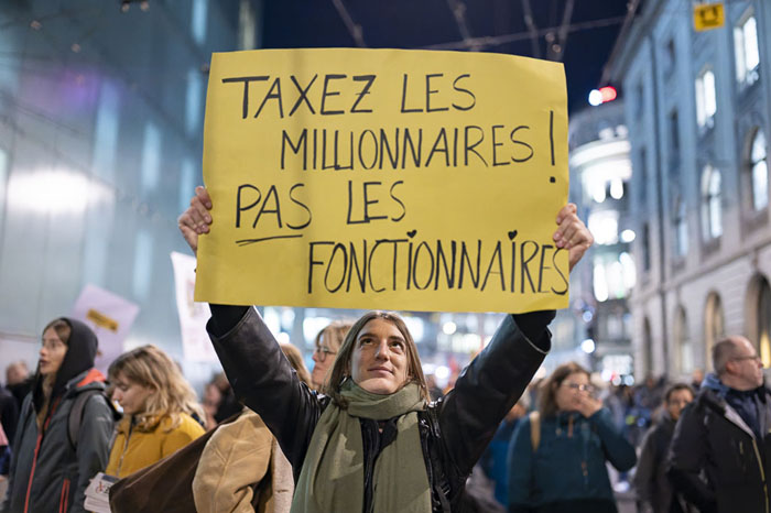 Manifestante tenant une pancarte « Taxez les millionnaires, pas les fonctionnaires » lors d’une grève de la fonction publique à Genève
