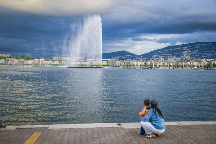 Vue sur le Jet d’eau de Genève et la rade, avec une mère et son enfant au bord du lac Léman